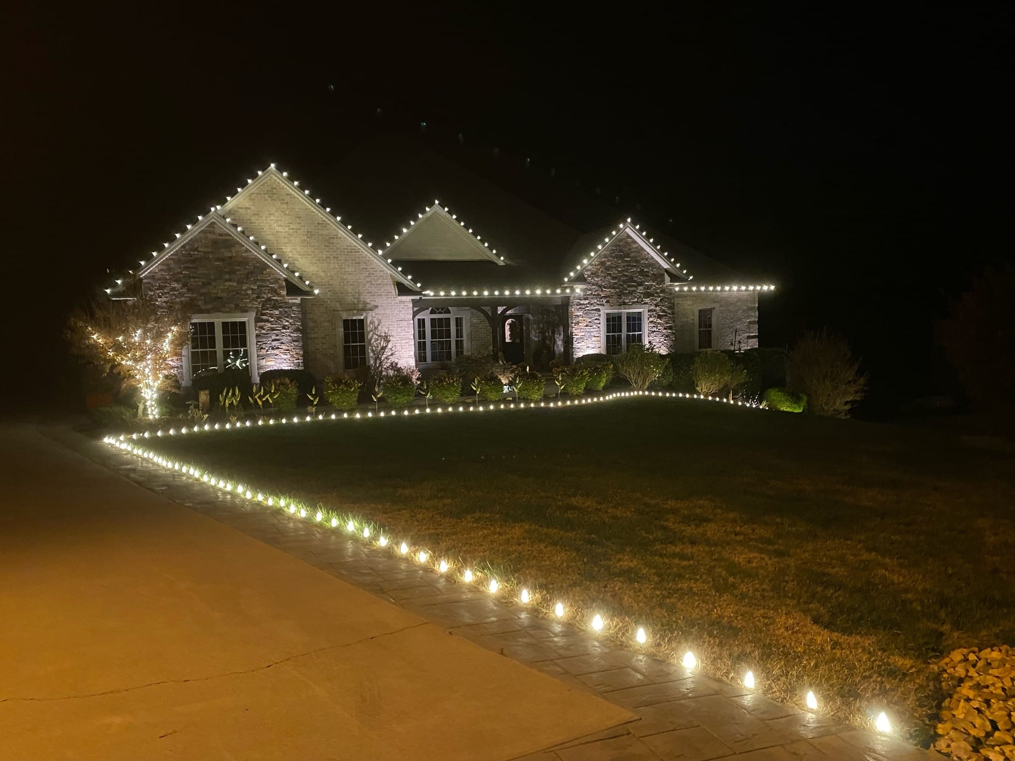 House illuminated with Christmas lights, a perfect example of Christmas light ideas. Lights line the roof, bushes, and walkway, creating a warm, inviting holiday scene.