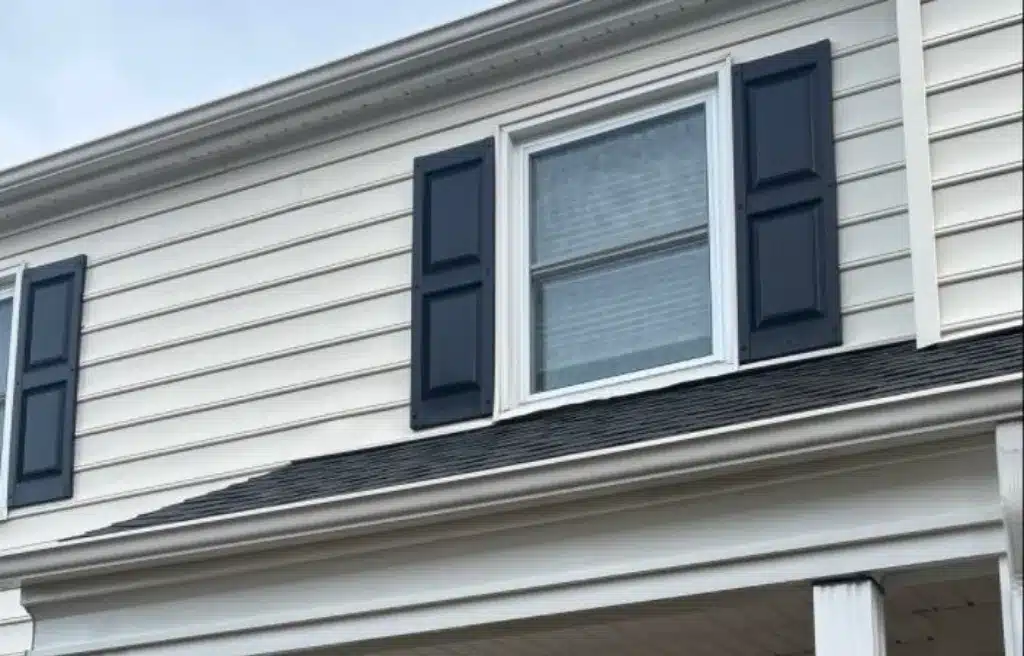 Exterior of a home with white siding and dark blue shutters framing a window. Illustrates how freezing temperatures can affect siding, brick, and concrete.