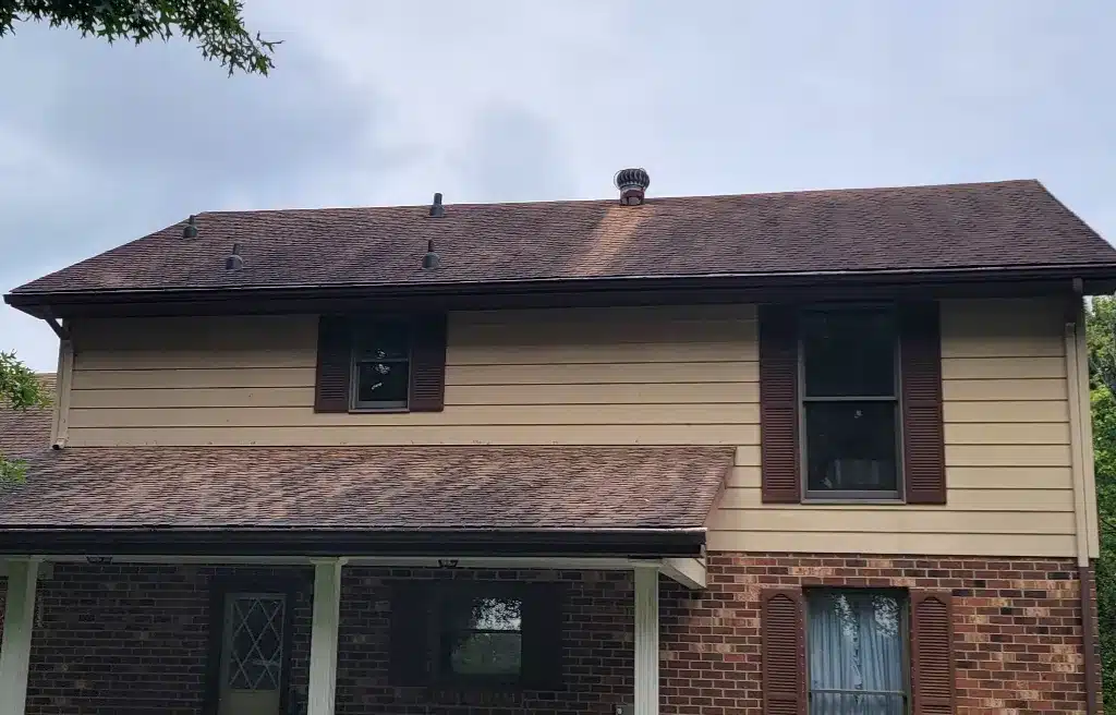 Two-story house with brown shingle roof, tan siding, and brick foundation. Winter house washing is a smart move to prep for spring.
